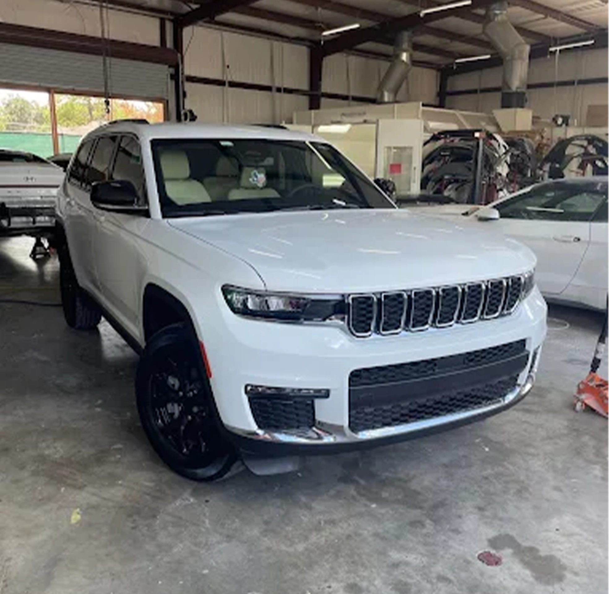 Freshly repaired white SUV parked inside an auto body shop, showcasing a clean front end and detailed finish after collision or paint work.